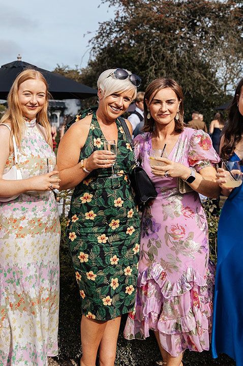 Wedding guests wearing assorted colourful dresses standing in a line posing for picture 