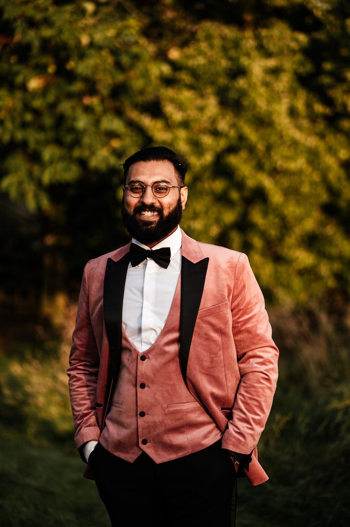 A groom wears a dark pink tuxedo with black lapel.