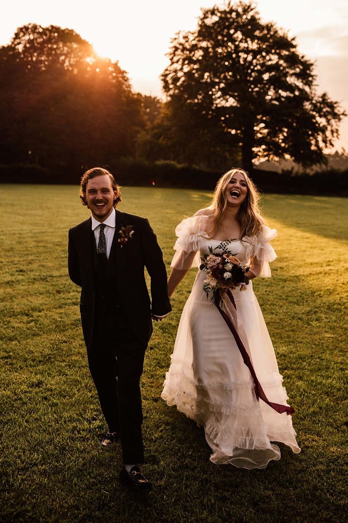 Bride in off shoulder ruffled wedding dress with floral bouquet and groom in tux 