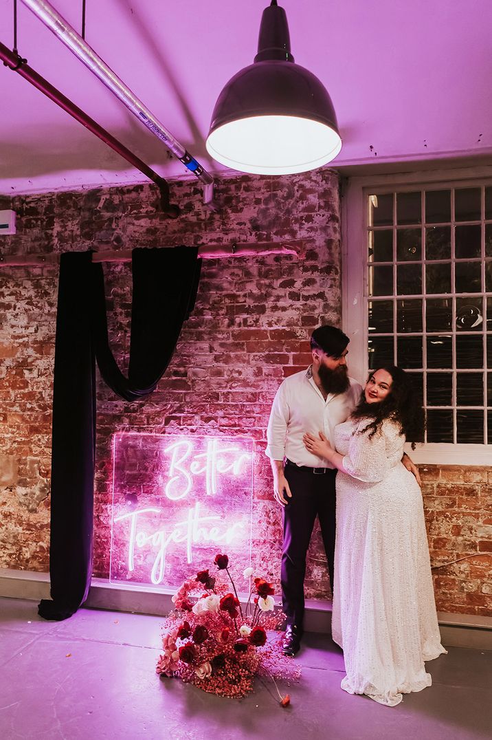 Bride and groom pose in front of a pink neon sign reading 'Better Together'