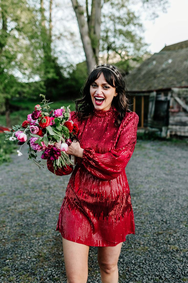   Bride in a short red shimmery Rixo dress with long sleeves for the wedding reception with a colourful bouquet 