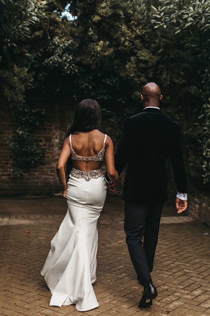 Black bride in wedding reception dress with embellishments and cut out detail walking with the groom 