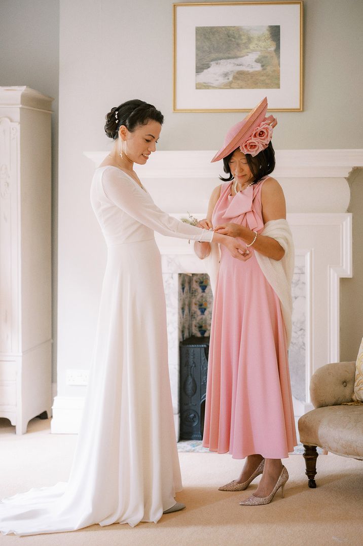 Mother of the bride in light pink wedding outfit helping the bride get ready for the wedding day 