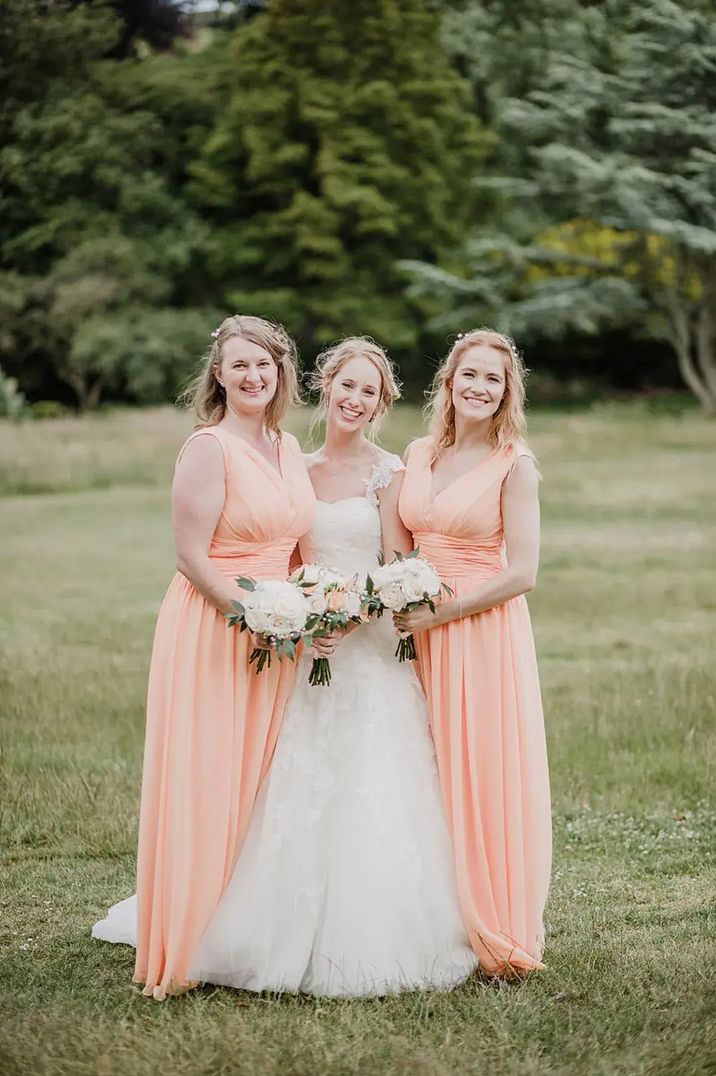 Bridesmaids wearing peach bridesmaid dresses standing either side of the bride