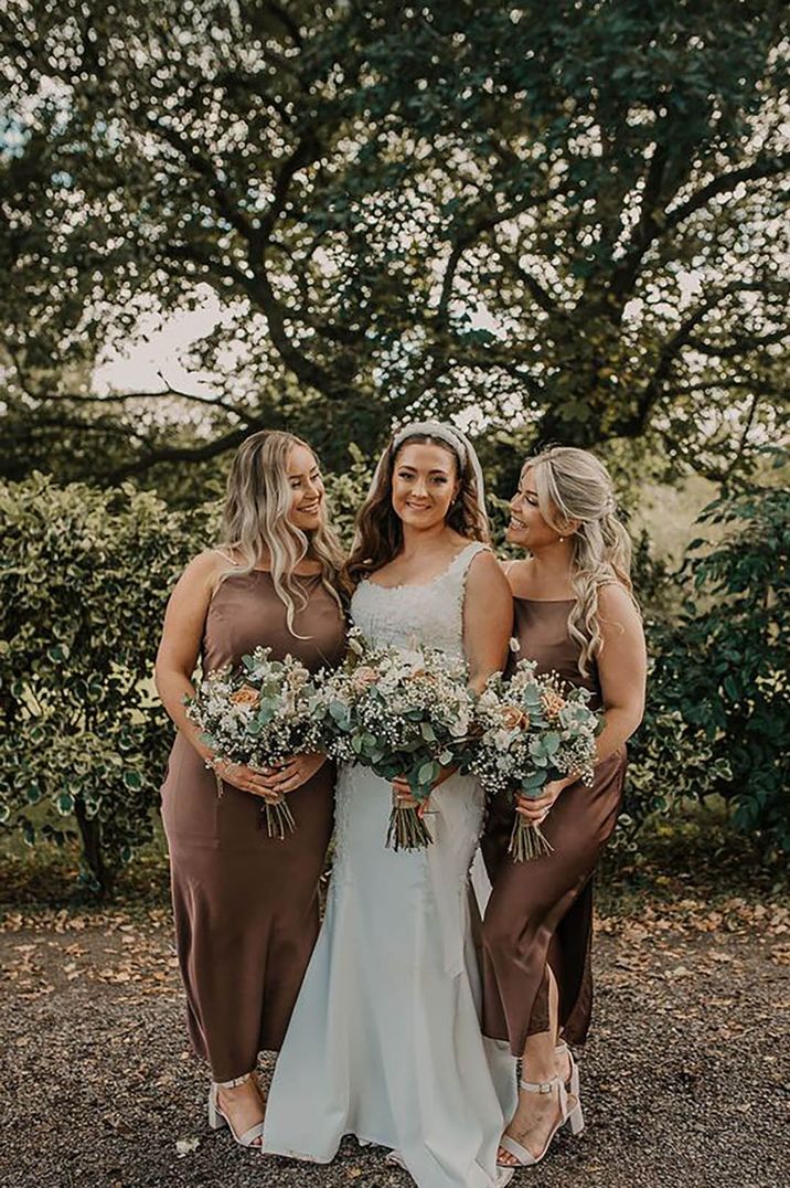 Bride smiling for a picture with two bridesmaids wearing brown bridesmaid dresses by Pink Wave Photography 