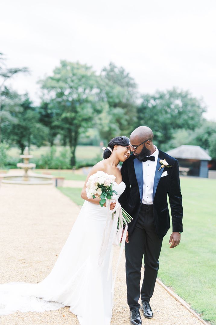 Classic bride in a strapless wedding dress holding a rose bouquet as she leans on her grooms shoulder in a black tuxedo 