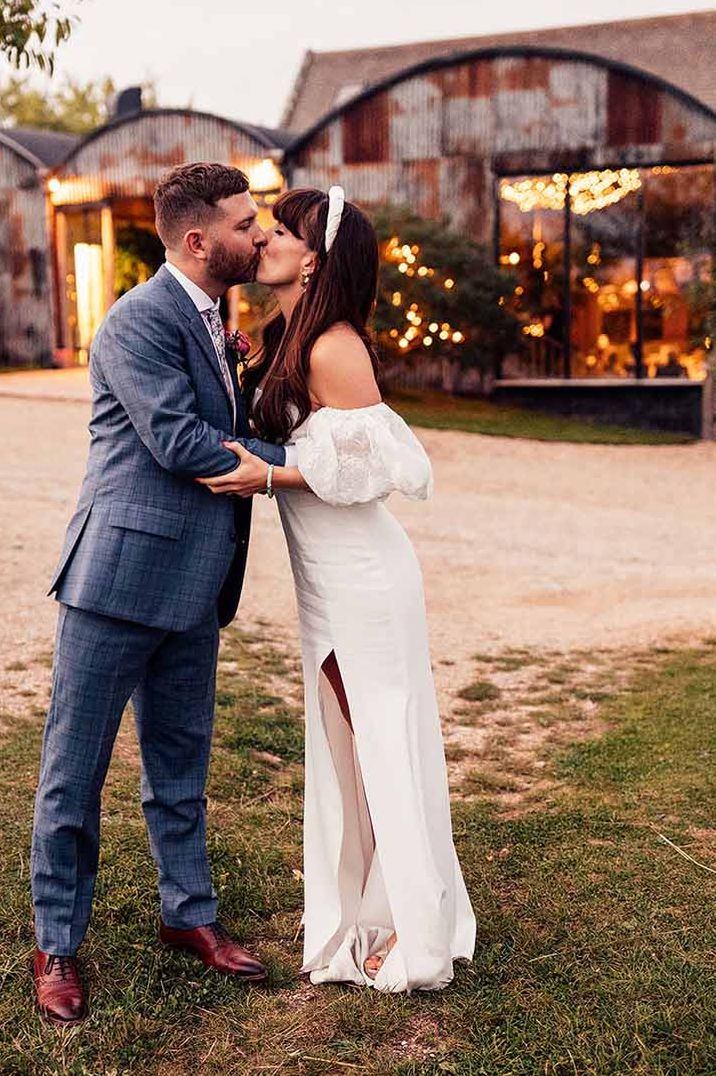 Bride in puff sleeve off shoulder wedding dress and groom in navy checkered suit kissing at Stone Barn