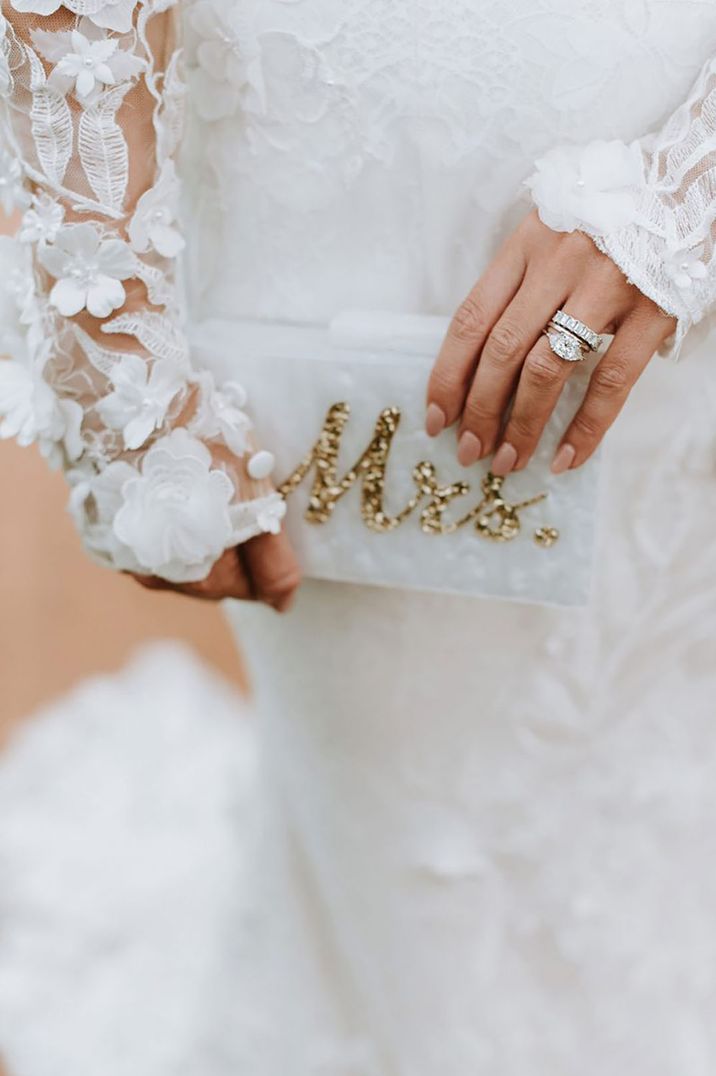 Bride holds white clutch with gold glitter Mrs to the front 