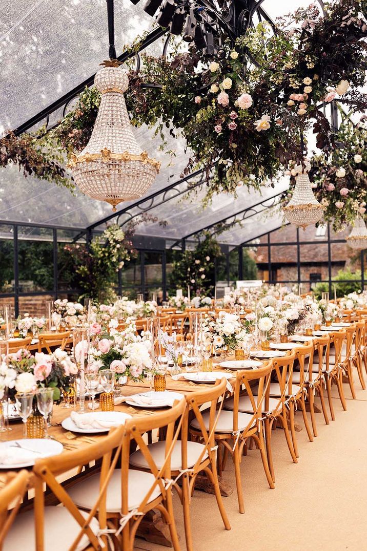 Stunning wedding over 60k with at home glass marquee decorated with floral installation and chandeliers with pink and white flower arrangements lining the tables 