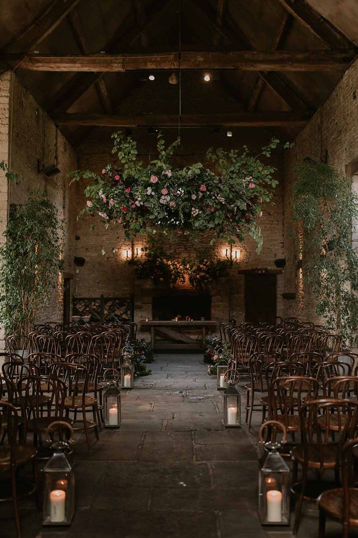 Reception room of Cripps Barn wedding venue with suspended foliage wedding decor, pillar candles down the aisle and festoon lighting 