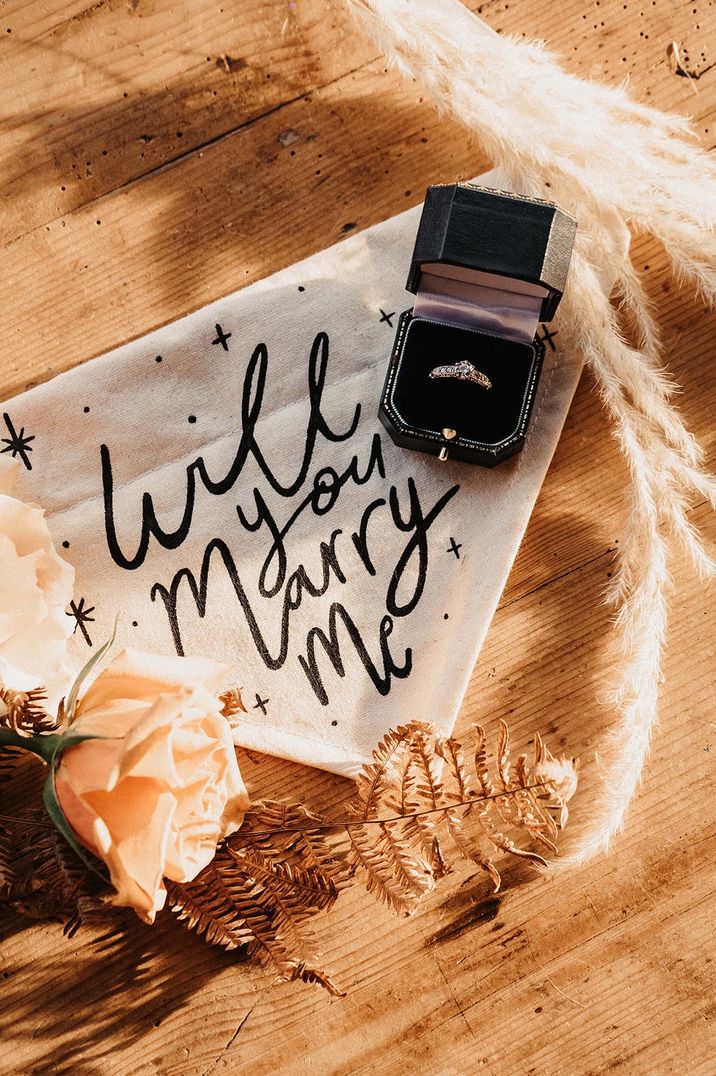 Handpainted black and white 'will you marry me?' banner sign with ring box with engagement ring inside 