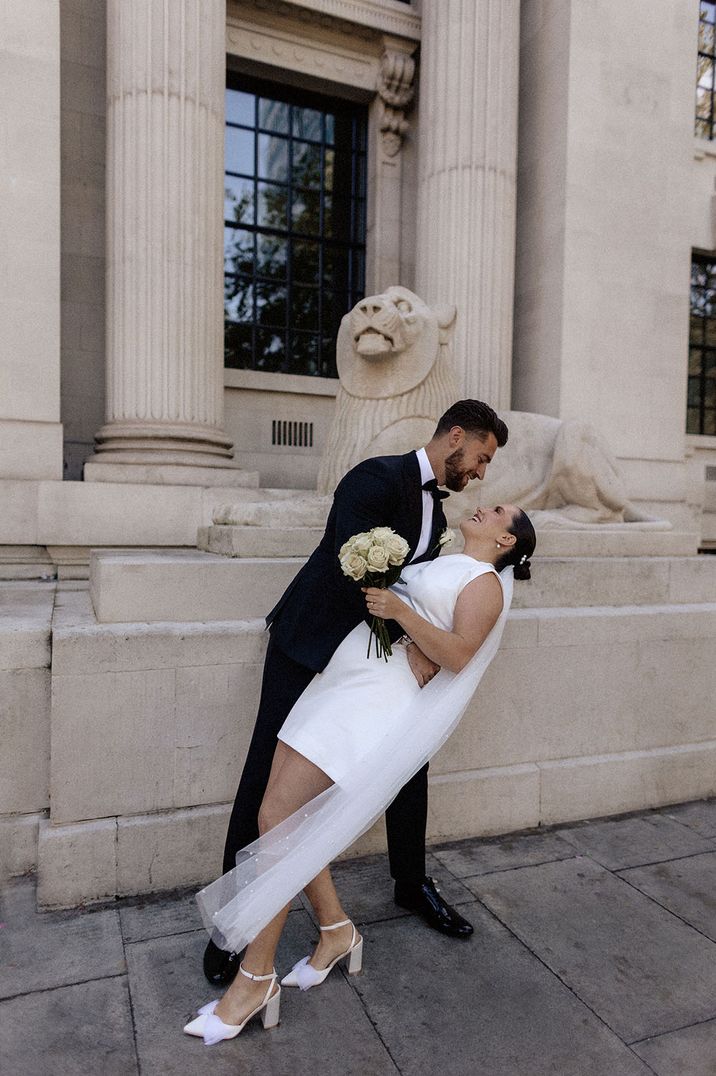 Groom holding bride, both posing outside registry office wedding