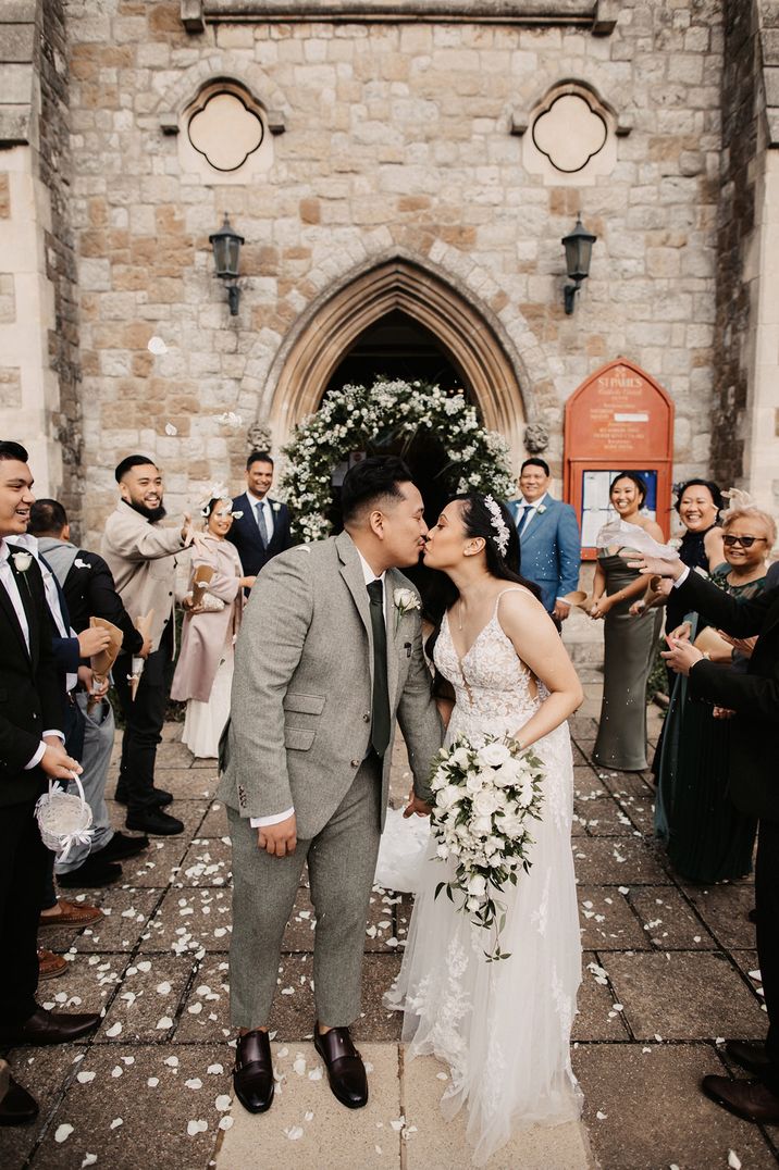 Bride and groom kissing outside the church with the bride holding a white rose cascading wedding bouquet 