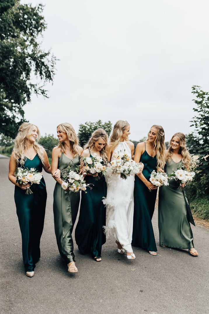 Bride in satin wedding dress walks with bridesmaids in assorted green satin Rewritten bridesmaid dresses