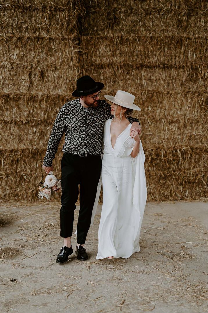 Groom in patterned shirt and black hat with bride in white wedding dress with cream hat 