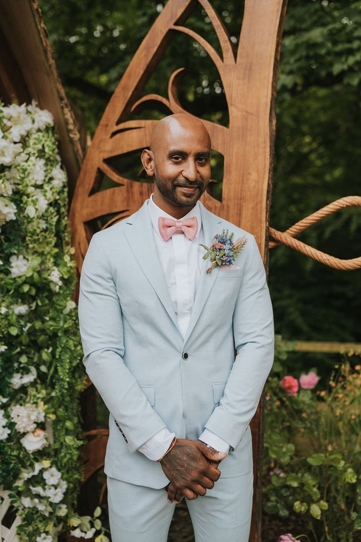 Groom in a light blue suit with a pink bow tie and pastel flower buttonhole 