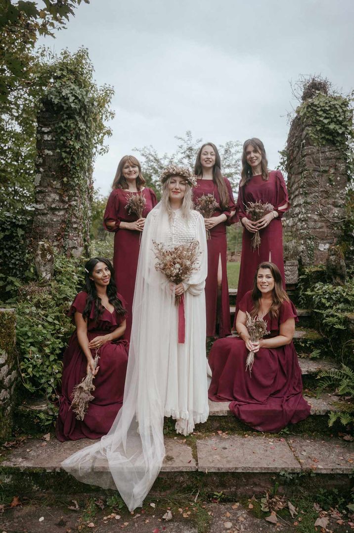 Bride in long sleeve lace wedding dress with church length veil standing with bridesmaids in burgundy mid length sleeve bridesmaid dresses at Pagan wedding