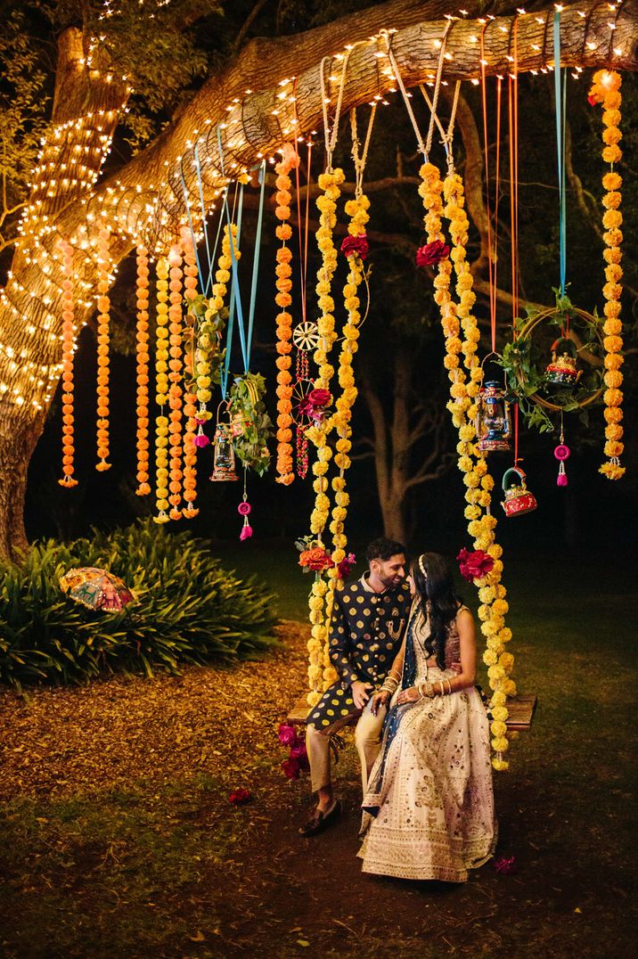 Sri-Lankan and Indian wedding with bride and groom sitting on a swing under colourful streamers and lights 