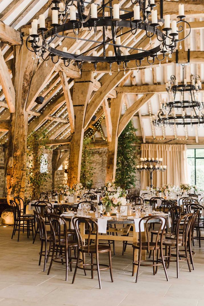 Wedding reception room with large three tiered candle chandeliers, fairy lights and large wooden beams