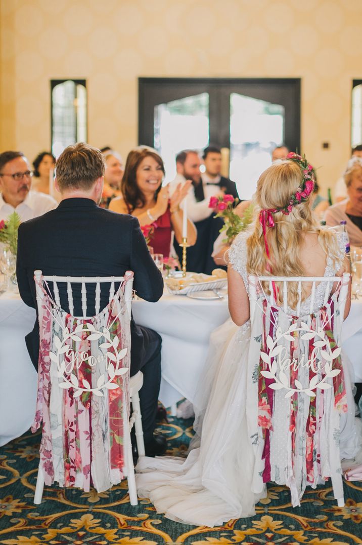 Different coloured and patterned fabric ribbons tied together to decorate the bride and groom's chair with white signs 