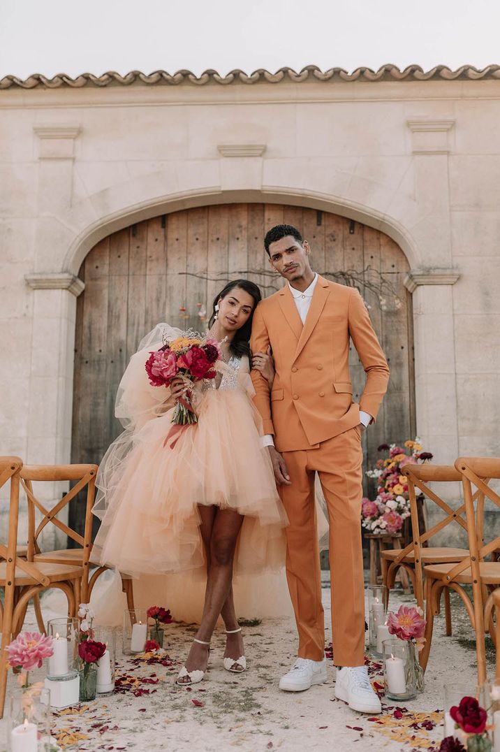 Bride in tulle orange wedding dress with groom in double breasted orange suit 