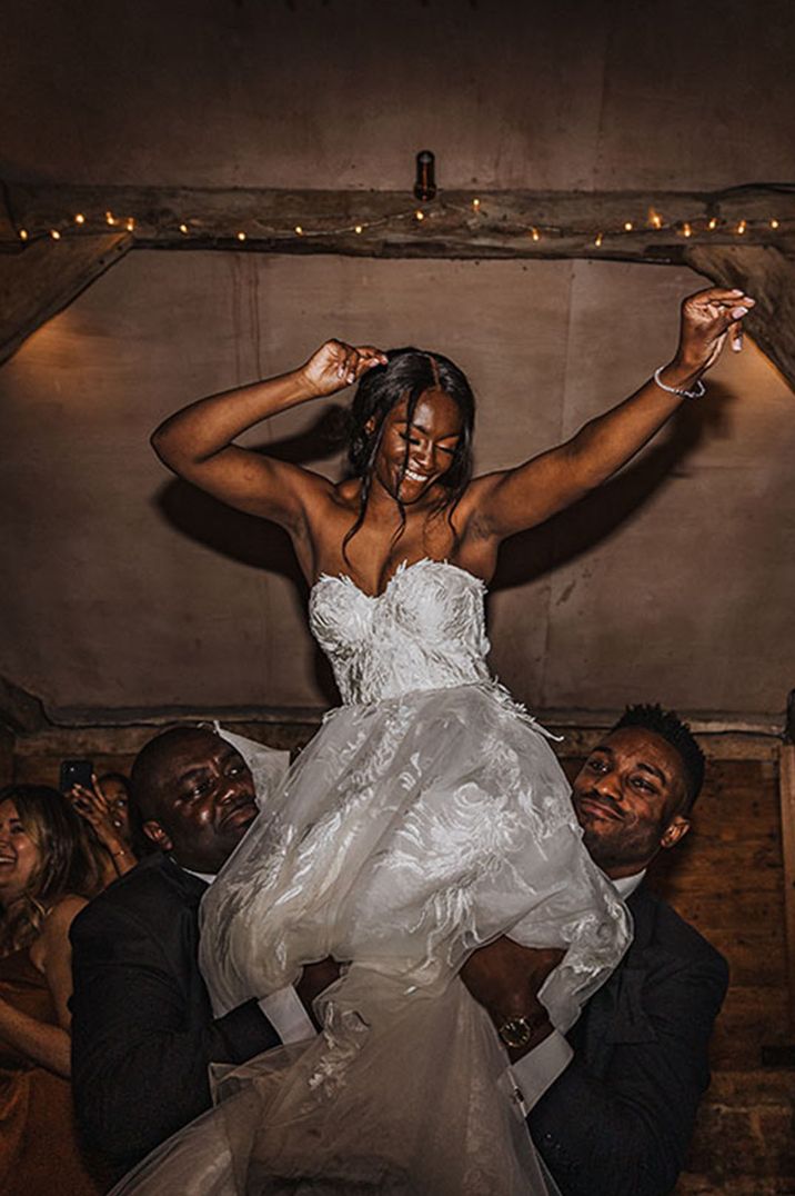 Bride in strapless wedding dress dancing on the shoulders of the groomsmen 