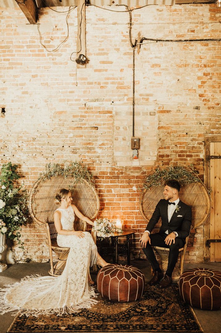 Bride in a Grace Loves Lace fringe wedding dress sitting on a wicker peacock chair with her husband 