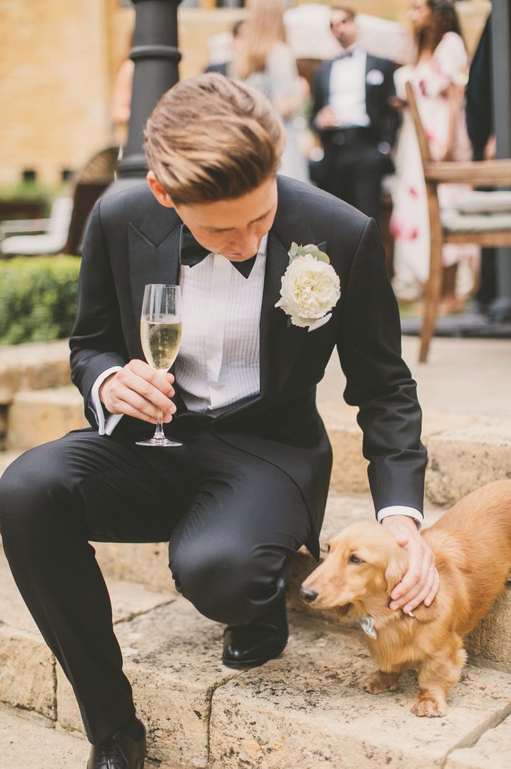 Groom on a tuxedo petting his pet dachshund at his classic wedding 