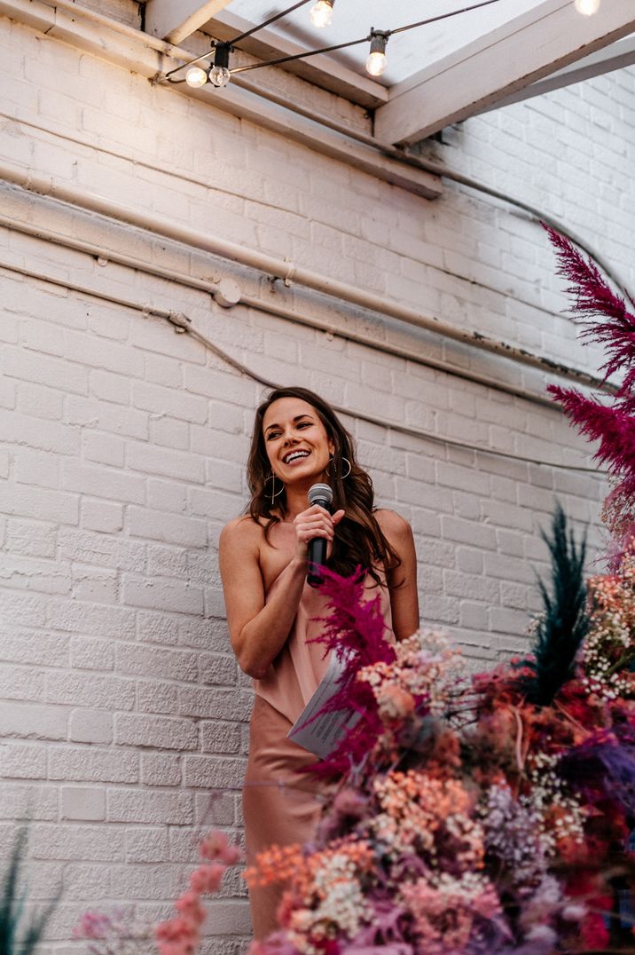 Person giving wedding speech in pink ruffled wedding dress on floral staircase