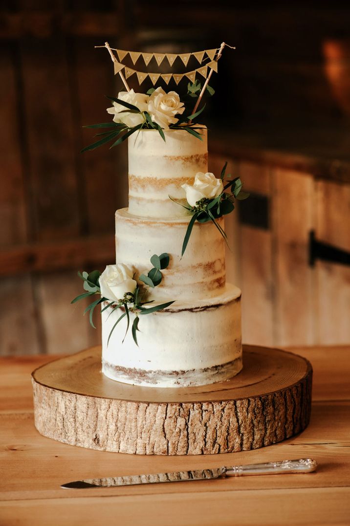 Three tiered buttercream wedding cake with green flower decorations and bunting wedding cake topper 