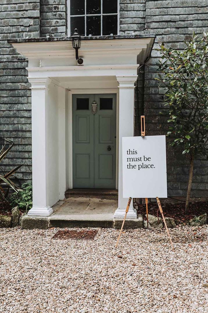 Grey door at Treseren wedding venue with white "this must be the place" minimal wedding sign on wooden easel