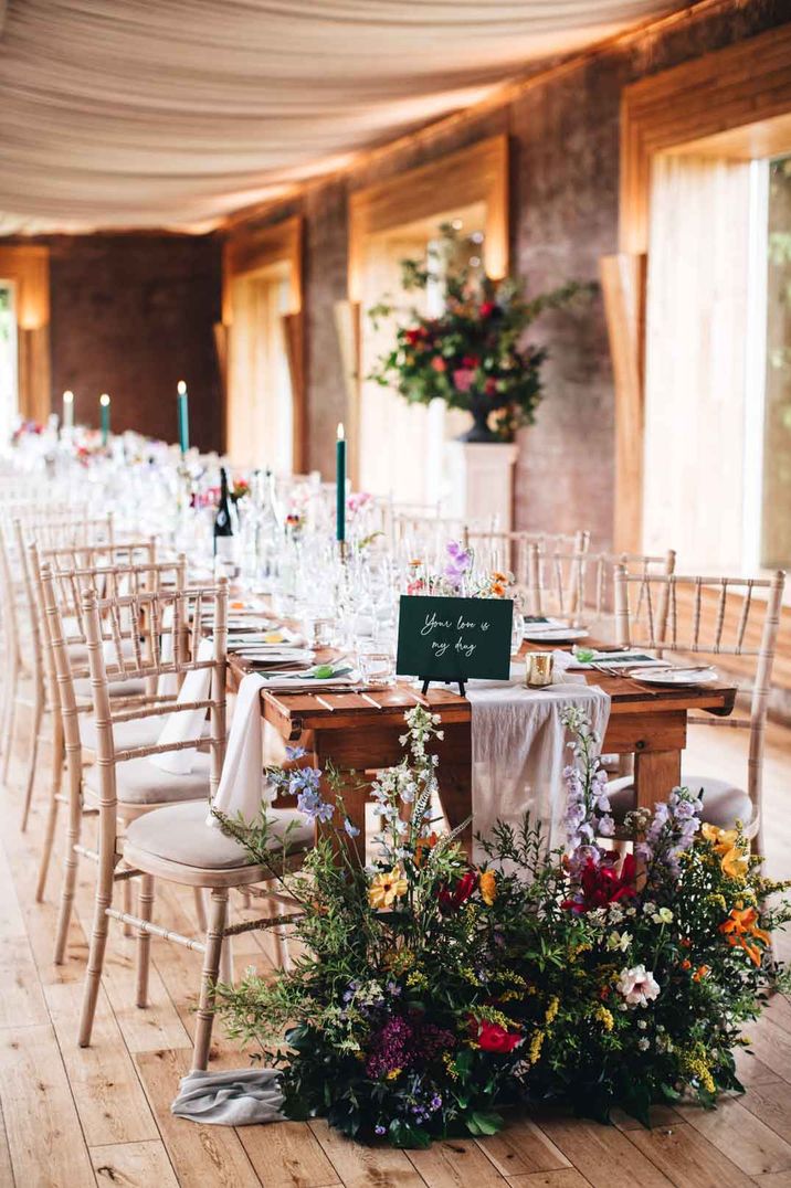 Classic wedding tablescape at Elmore Court wedding venue with light linen table runners, forest green tapered candles and colourful flower and foliage floral arrangements 