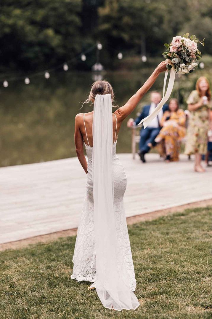 Bride in thin strap satin lace wedding dress doing wedding bouquet toss with stylish personalised veil