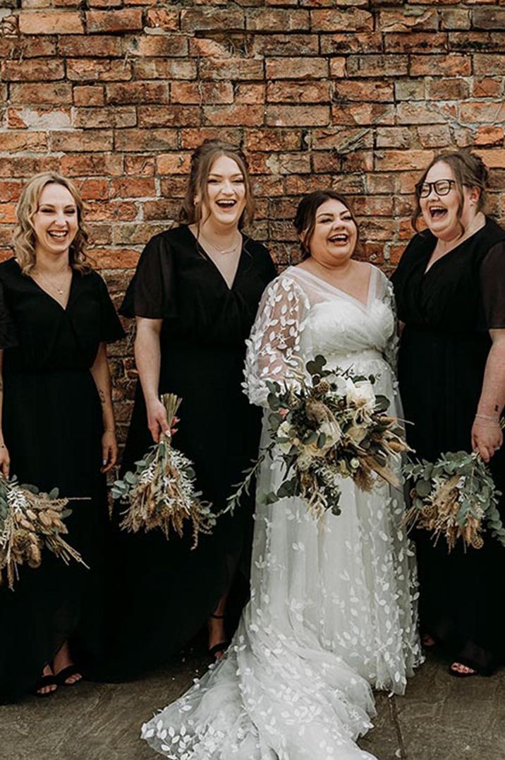 Bridal party in black bridesmaid dresses with bride in lace boho dress