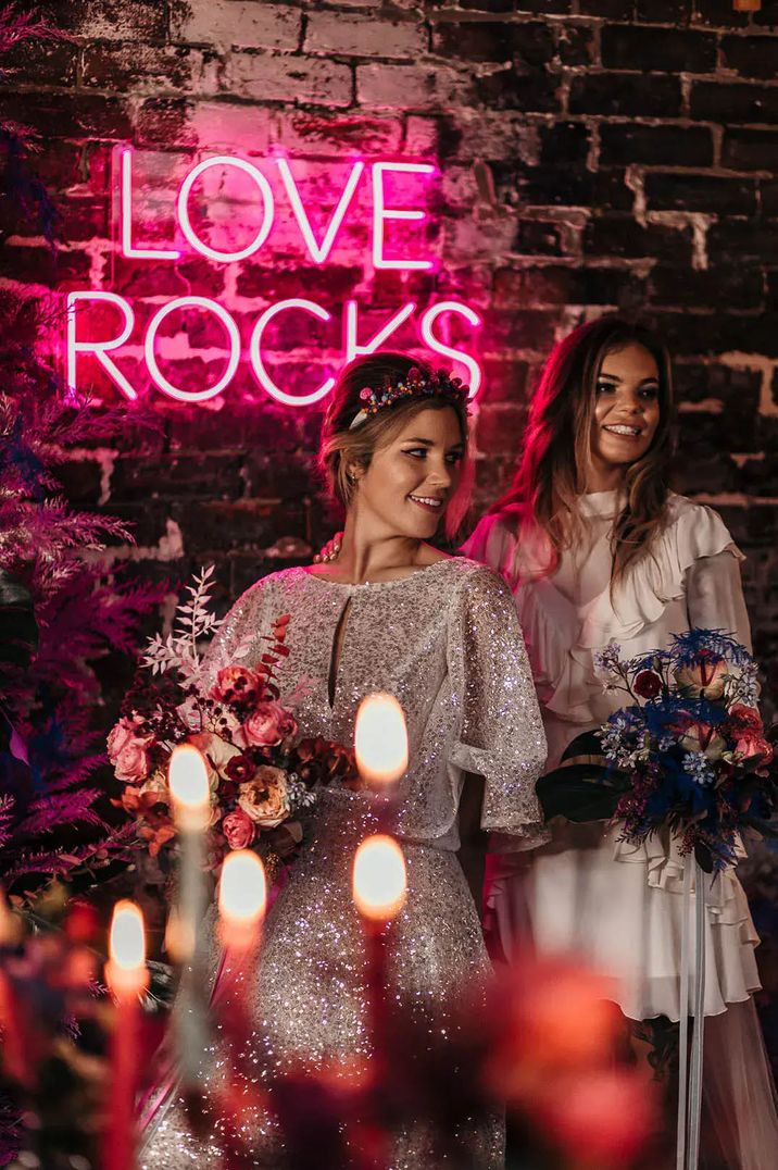 Two brides standing in front of a pink "love rocks" neon light by Leanne Peacock Photography