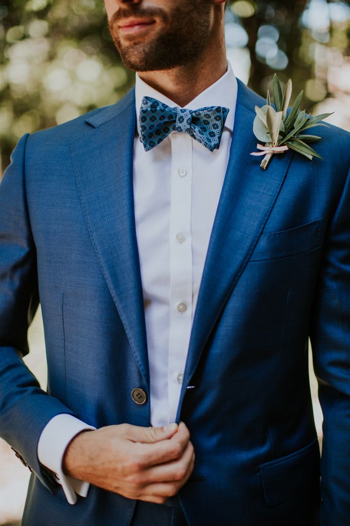 Groom in a blue suit with blue patterned bow tie with an olive lead foliage wedding buttonhole