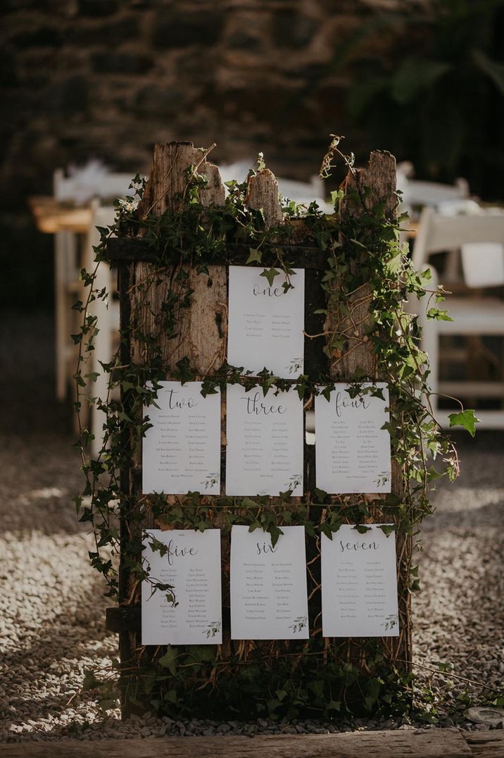 Rustic wooden table plan with white and black place cards and ivy foliage decor 