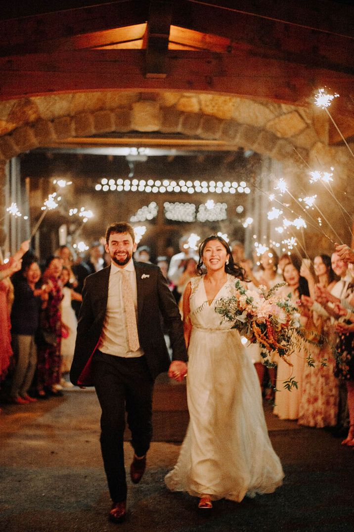 Bride and groom with linked hands walk through their wedding guests for their sparkler send off 