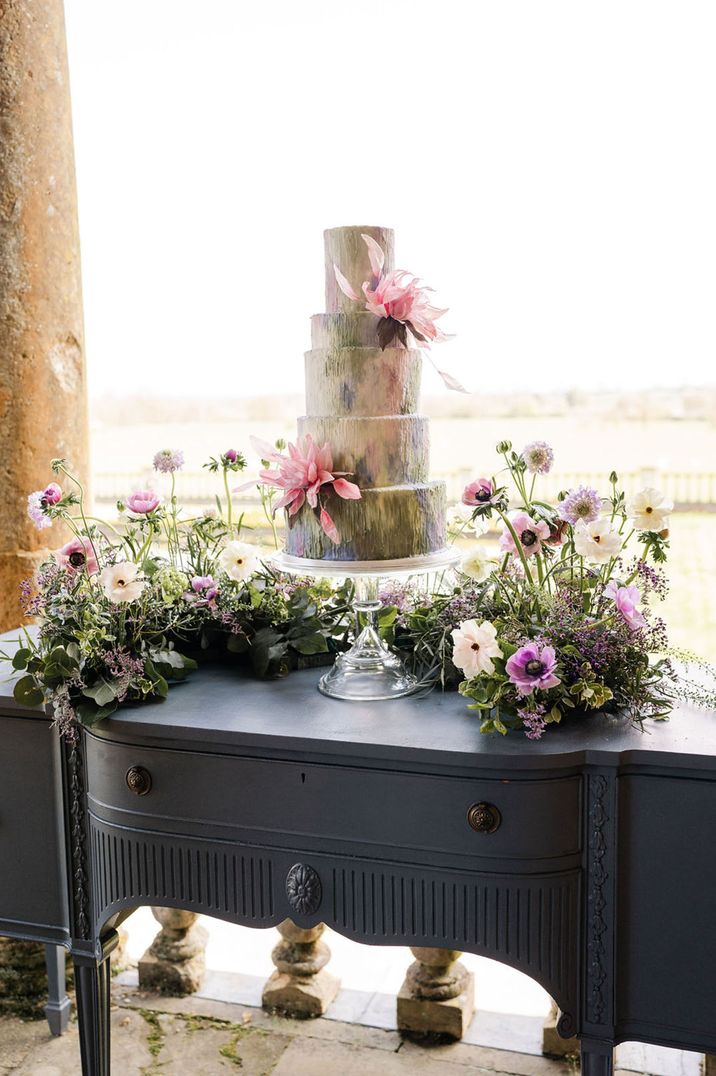 Epic six tier grand wedding cake design with green, purple, and pink icing and large pink wafer flowers 