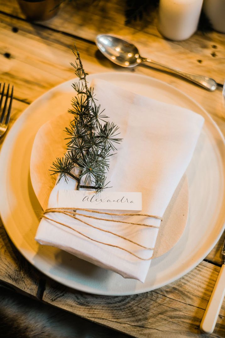 White Christmas wedding tablescape with white plates and napkin with mini evergreen sprig decoration for winter 