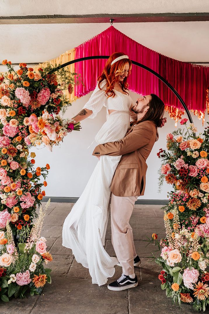 The groom lifts the bride up standing with bright flower columns 