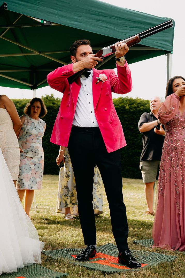 Groom in hot pink velvet suit jacket doing clay pigeon shooting for entertainment 