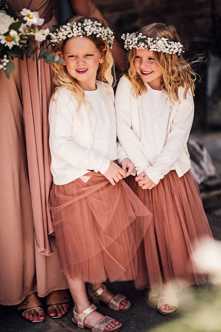 Two flower girls wearing pink tulle flower girl dresses with white cardigans 