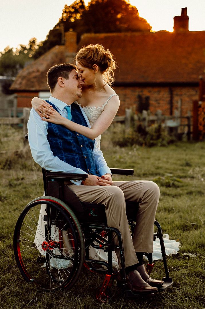 Bride in a lace wedding dress embracing her disabled groom in a wheelchair at their Southend Barns wedding 