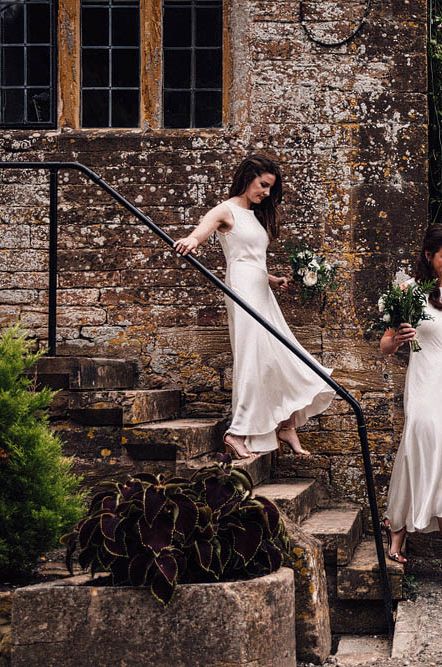 Bridesmaids in long satin white bridesmaid dresses helping bride with her long lace veil