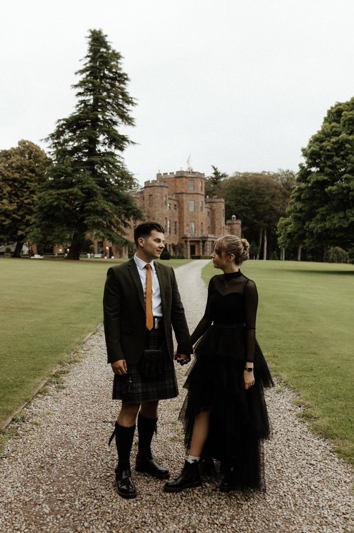 Bride in a long sleeve black wedding dress with a tulle layered skirt with the groom in a kilt and green suit jacket