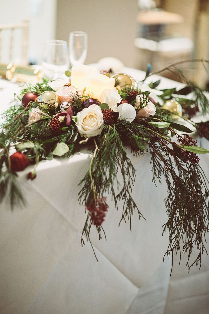 Table decor with foliage, pillar candles, and Christmas baubles for a winter wedding 