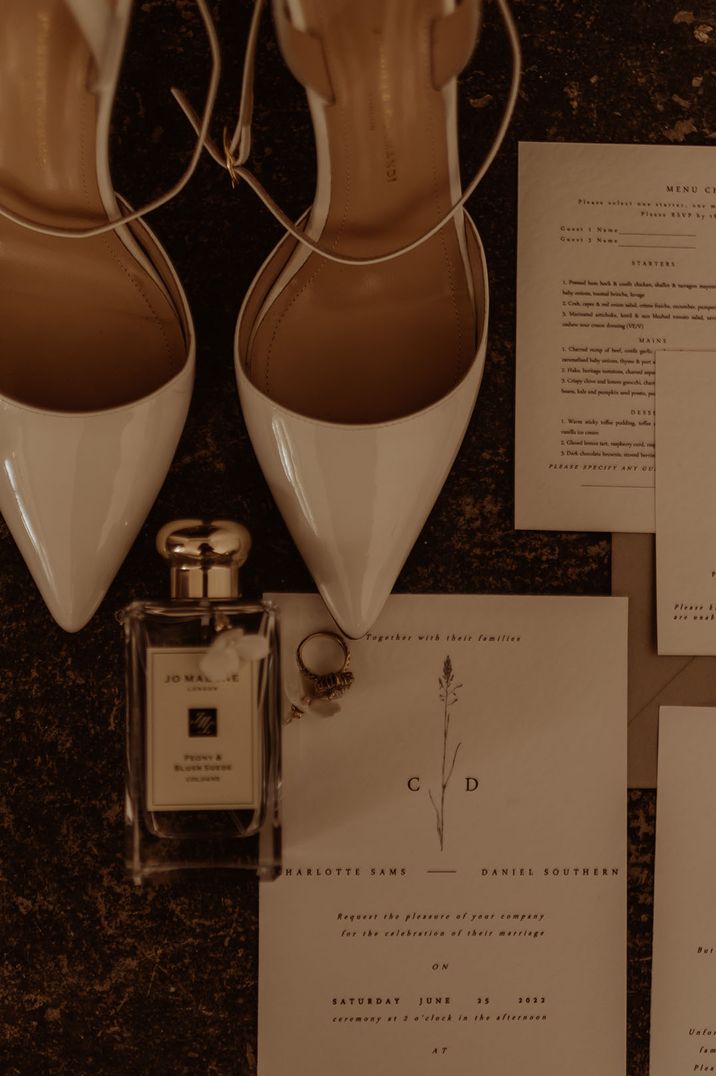 Pointed white wedding shoes and classic white wedding stationery with a bottle of Jo Malone wedding scent cologne 