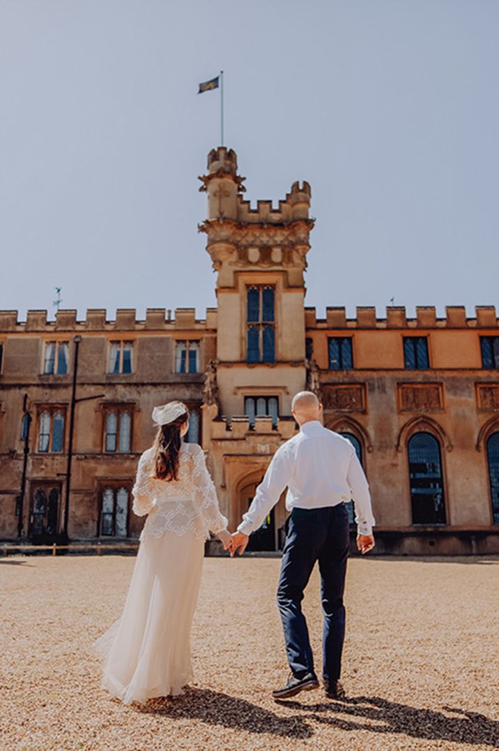 Bride in long sleeve lace wedding dress with hat with the groom in white shirt and blue trousers at country house wedding venue 