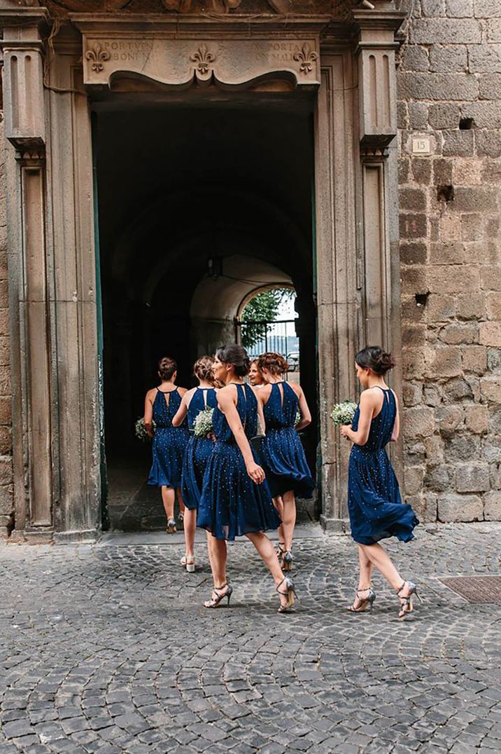 Bridesmaids wearing knee length blue dresses and holding bouquets entering historic venue at destination wedding by Studio AQ Photography 